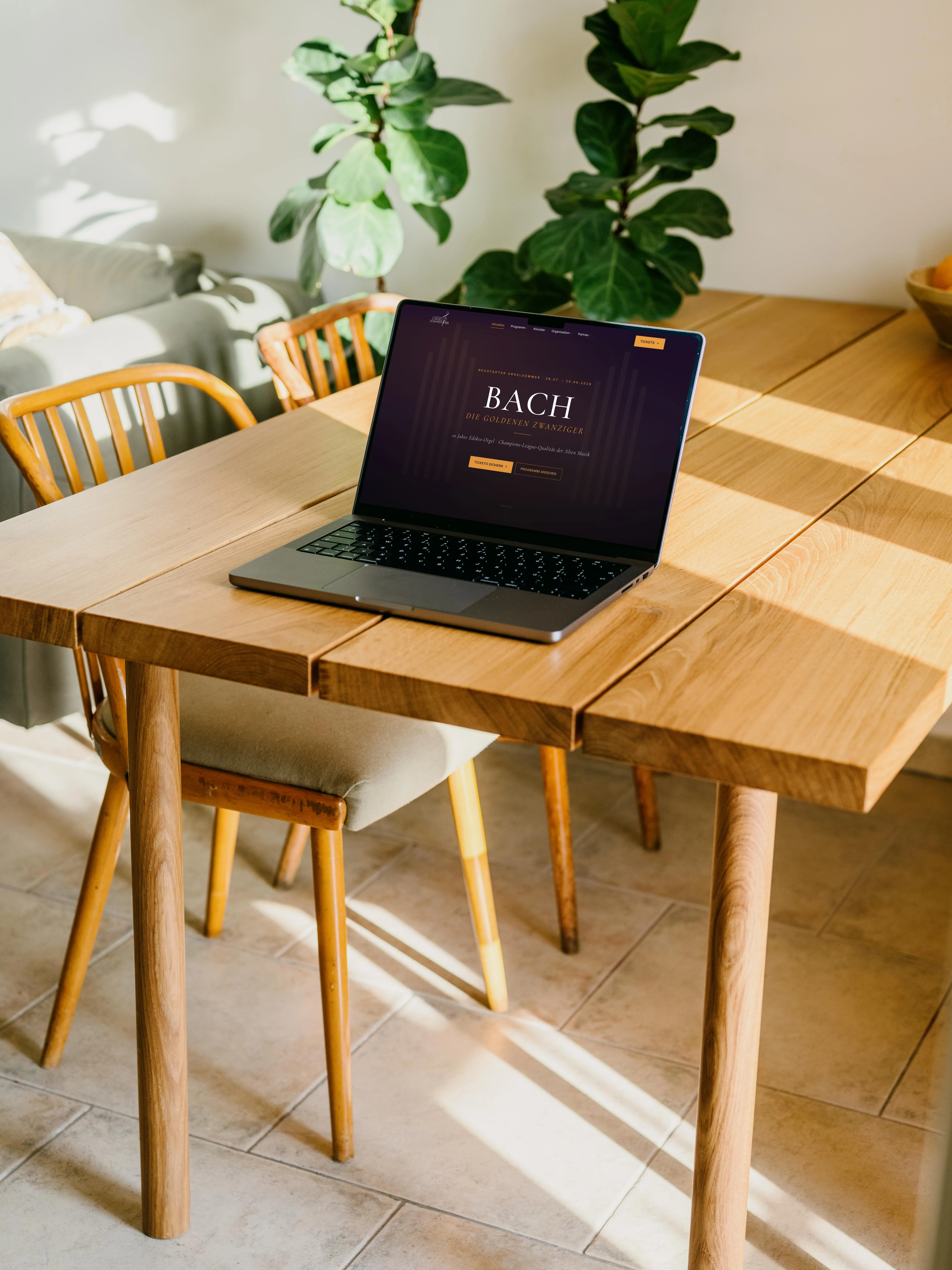 MacBook auf einem Eichentisch in warmem Sonnenlicht, auf dem Bildschirm die Startseite des Neustadter Orgelsommers